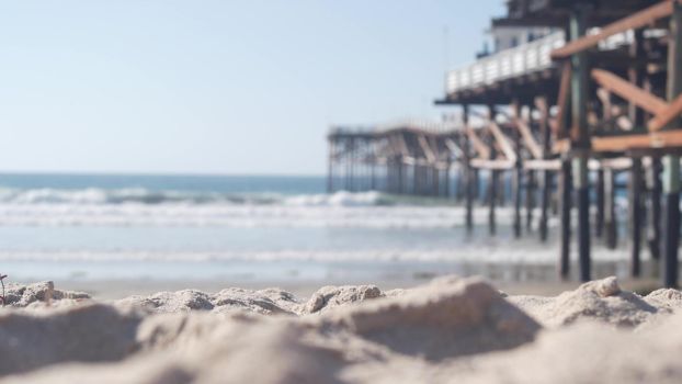 Below wooden Crystal pier on piles, ocean beach water waves, California USA. Summer vacations on Mission beach, San Diego shore. Under waterfront promenade on sea coast. Seamless looped cinemagraph.