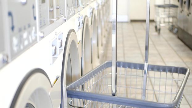 Row of washing and drying machines, public coin laundry in California, USA. Drums of washers and dryers in self-service laundromat or commercial laundrette. Automatic launderette in United States.