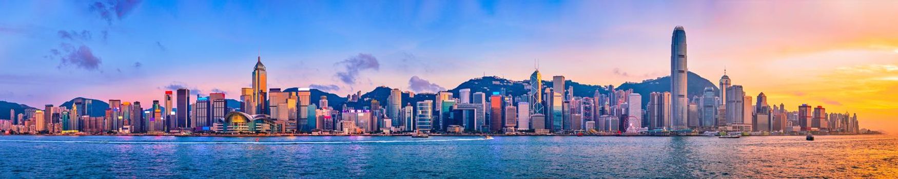 Panorama of Hong Kong skyline cityscape downtown skyscrapers over Victoria Harbour in the evening with junk tourist ferry boat on sunset with dramatic sky. Hong Kong, China