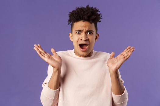 Close-up portrait of displeased, bothered frustrated hispanic man spread hands sideways in dismay and confusion, staring camera upset with disappointed grimacing expression, purple background.