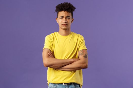 Close-up portrait of skeptical, unimpressed young man with dreads, look judgemental and uninterested, cross arms chest, go on impress me, smirk disappointed, purple background.