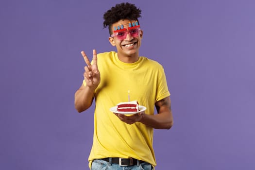 Celebration, party and holidays concept. Portrait of lovely charismatic hispaic guy in b-day glasses, celebrating his day, show peace sign photographing with birthday cake and lit candle, smiling.