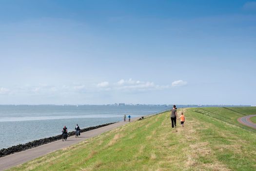 oudeschild, netherlands, 19 july 2021: people walk and ride bicycle on dike near oudeschild on the dutch island of texel under blue sky in summer in the netherlands