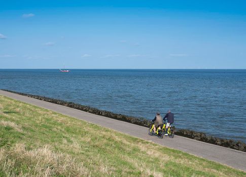 oudeschild, netherlands, 19 july 2021: couple rides bicycle on dike of wadden sea on dutch island of texel in summer under blue sky in holland
