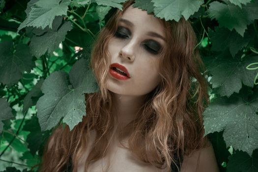 Portrait of beautiful young woman with red lips staying in front of green leaves