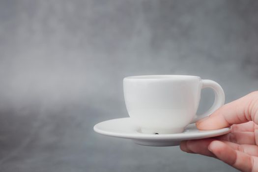 Hand holding white cup of coffee with saucer with copy space on dark background for drinks and beverage concept