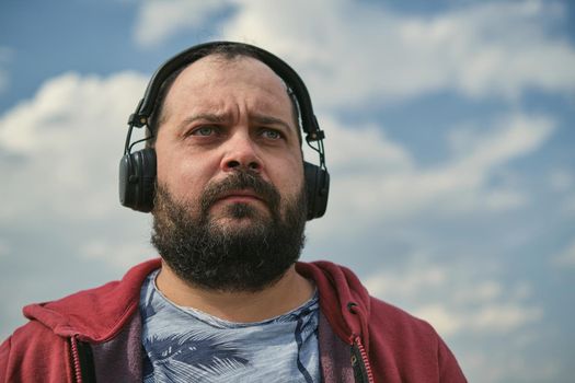 Middle-aged European man in headphones outdoors listening to music against the background of the sky