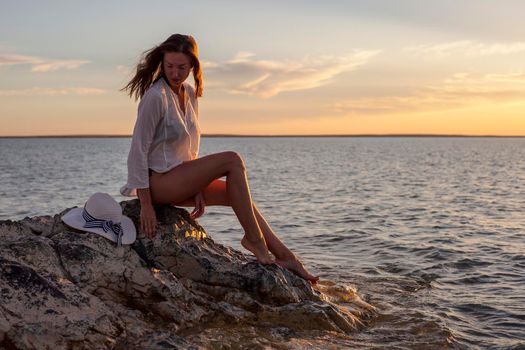 Beautiful woman enjoying sunset on the beach, sitting on rocks