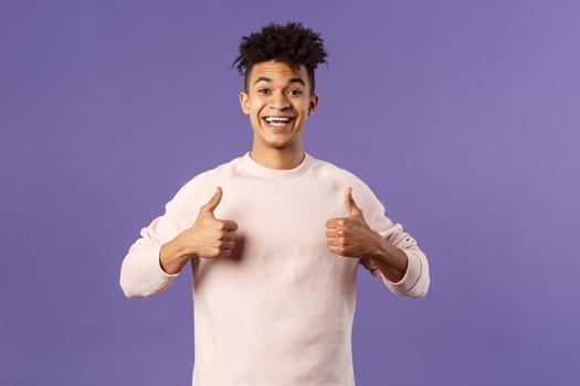 Portrait of upbeat, happy smiling man left pleased after using company service, studying at online language school, show thumbs-up and look camera, recommending, stand purple background.