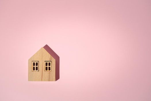 Wooden house model on pink background with copy space for housing concept