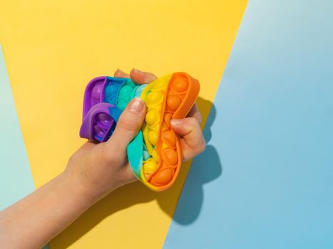 Female hand with popit toy clenched into fist, top view over blue yellow background. Popit on multicolor background. Popular silicone colorful antistress pop it child toy. from above. Simple dimple