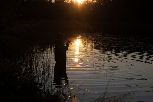 Night fishing. A fisherman at sunset is catching fish, out of focus.