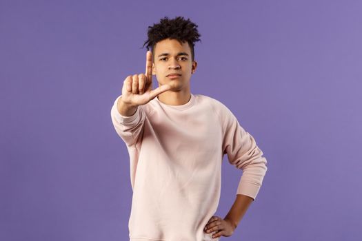 Not so fast, stop. Portrait of young serious-looking hispanic elder brother scolding sibling, forbid coming outside, shaking finger with serious confident face, prohibit action, purple background.