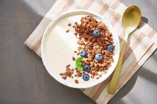 Yogurt with chocolate granola, bilberry. Breakfast on brown table, top view, sun light