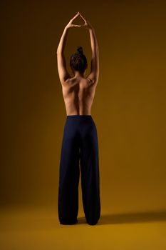 Back view of sporty female practicing yoga pose at studio. Flexible girl with bar back standing, raising hands together, meditating. Isolated on yellow studio background.