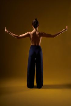 Back view of brunette with hair bun doing yoga at studio, Flexible woman standing with bare back. raising arms, palms up, wearing sport suit, Concept of new age and yoga.