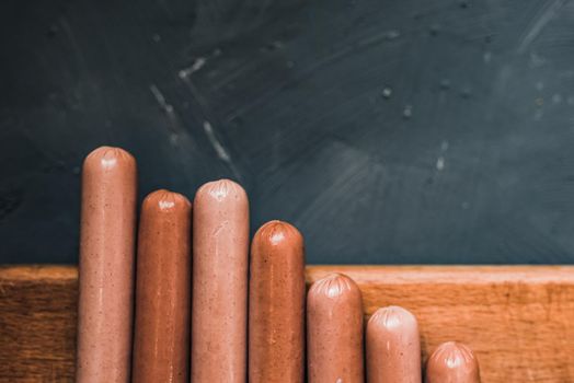 Boiled fried sausages sausages lie on a wooden kitchen board scratched against a dark concrete background.