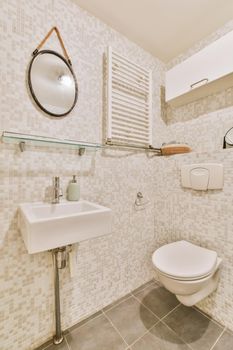 Modern toilet installed on beige wall under button and sink under mirror in light bathroom at home