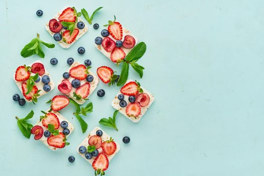 vegeterian dieting rise crispbread with berries: strawberry, blueberry, bilberry, blackberry and banana on pastel turquoise aquamarine background top view