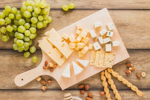 green grapes almonds bread sticks cheese blocks chopping board wooden desk