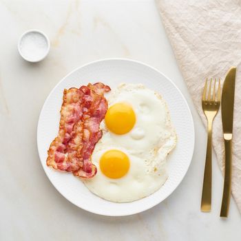 fried eggs with bacon, foodmap ketogenic keto diet, top view, background fork knife towel and salt