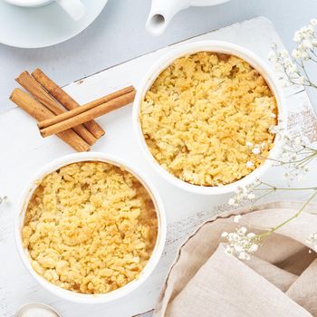 Apple crumble with streusel on light gray table. Morning breakfast with flowers.