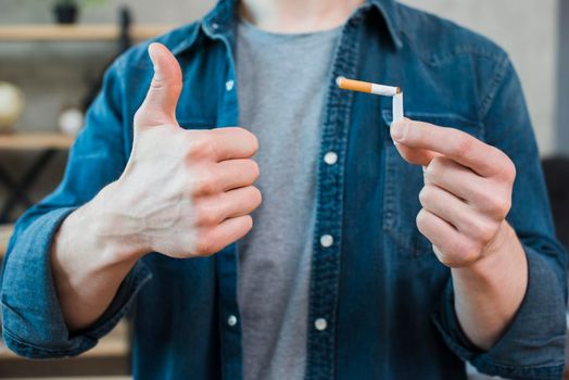 man holding broken cigarette showing thumb up gesture