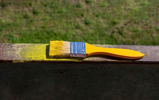 The yellow brush is lying on the rusty metal railing on the balcony on a sunny day. Diy.