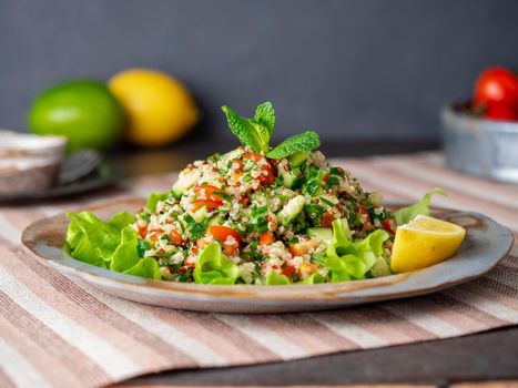 Tabbouleh salad with quinoa. Eastern food with vegetables mix, vegan diet. Side view, linen napkin, old plate