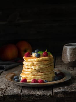 Pancake with butter, blueberries and raspberries. Side view, copy space, vertical. Dark moody old rustic wooden background.