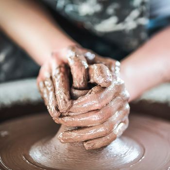 Woman making ceramic pottery on wheel, hands close-up, creation of ceramic ware. Handwork, craft, heavy dirty work