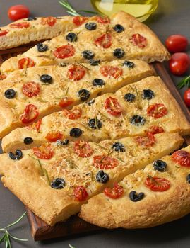 Focaccia, pizza, italian flat bread with tomatoes, olives and a rosemary on dark brown table, vertical