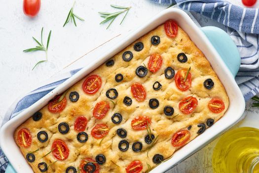Focaccia with tomatoes, olives and a rosemary in casserole, top view. Traditional Italian flat bread