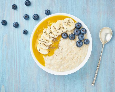 Oatmeal with bananas, blueberries, chia seeds, jam on blue wooden background. Healthy breakfast