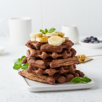 Chocolate banana waffles with maple syrup on white table, side view. Sweet brunch, a maple syrup flow.