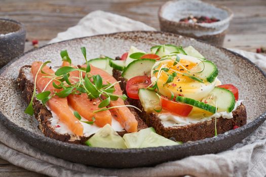 Smorrebrod - traditional Danish sandwiches. Black rye bread with a salmon, cream cheese, cucumber, tomatoes on a wooden table, side view, close up