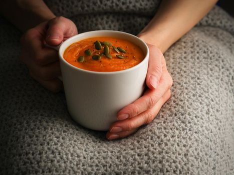 Pupmkin cream soup in hands, dietary vegetarian lunch. Side view. Dark photo.