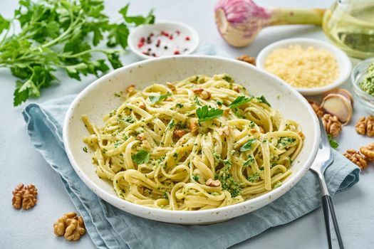Pesto pasta, bavette with walnuts, parsley, garlic, nuts, olive oil. Side view, close-up, blue background