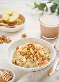 Oatmeal with apple, nuts, cinnamon, honey and cup of cocoa on white wooden light background. Vertical. Healthy diet breakfast