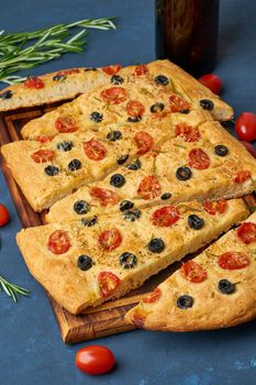 Focaccia, pizza, italian flat bread with tomatoes, olives and a rosemary. Dark blue background, side view