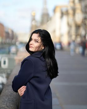 Portrait f beautiful intelligent brunette who walks down street of Saint-Petersburg in city center. Charming thoughtful woman with a long dark hair wanders alone, immersed in thoughts, back turned