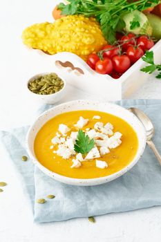 Pumpkin cream soup with feta cheese, autumn homemade food, white background, vertical closeup, seasonal vegeterian dish