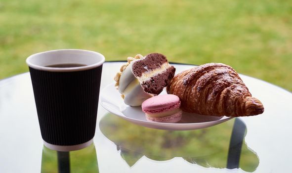 Breakfast with croissant and dessert, coffee or tea in plastic mug, in the village, outdoors, nature. Selective focus.