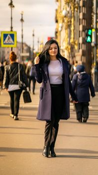 Beautiful serious smart brunette girl walking down street of St. Petersburg in city center. Charming thoughtful fashionable woman with long dark hair wanders alone