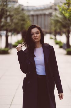 Beautiful serious smart brunette girl walking down street of St. Petersburg in city center. Charming thoughtful fashionable woman with long dark hair wanders alone
