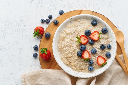 Oatmeal rustic porridge with blueberry, bilberry, blackberry, strawberry, dash diet, wooden white background top view copy space