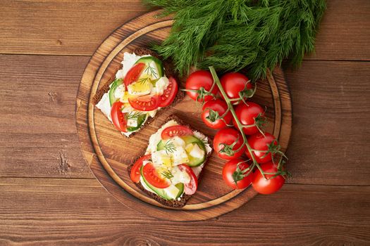 Smorrebrod - traditional Danish sandwiches. Black rye bread with boiled egg, cream cheese, cucumber, tomatoes on dark brown wooden background, top view