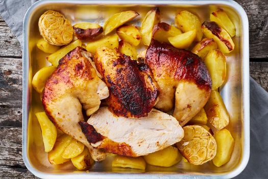 Grilled chicken meat, leg, thigh with baked potatoes, garlic. Top view, close up. Gray old wooden table.