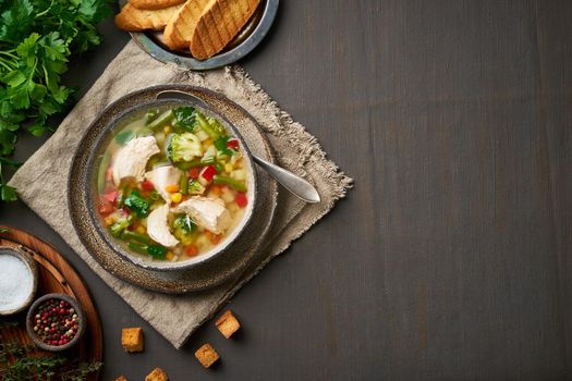 Homemade chicken soup with vegetables, broccoli on a dark brown background, top view, copy space