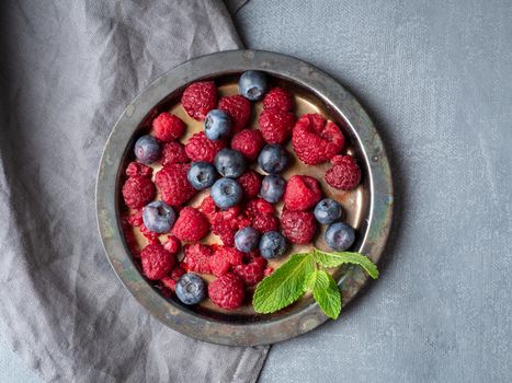 Blueberries and raspberries on plate. A mix of berries on dark background